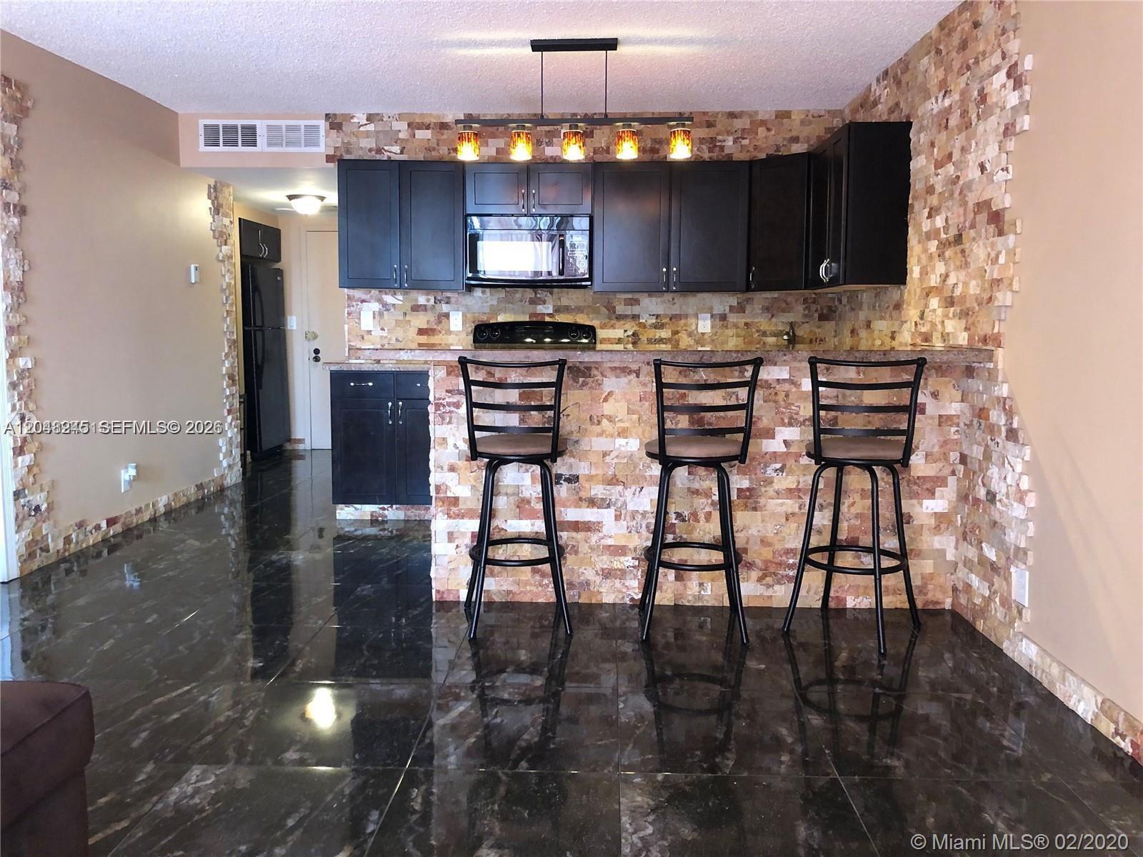 A kitchen features dark cabinets, a stone-tiled backsplash, a breakfast bar, and dark tile flooring — 600 SE Three Islands Blvd # 1018, Hallandale Beach FL 33009, HALLANDALE BEACH, FL
