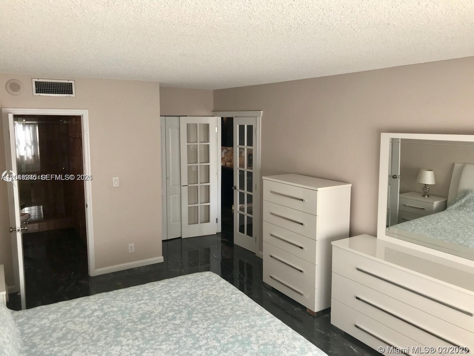 A bedroom features dark tile flooring, white furniture, and French doors leading to another room — 600 SE Three Islands Blvd # 1018, Hallandale Beach FL 33009, HALLANDALE BEACH, FL