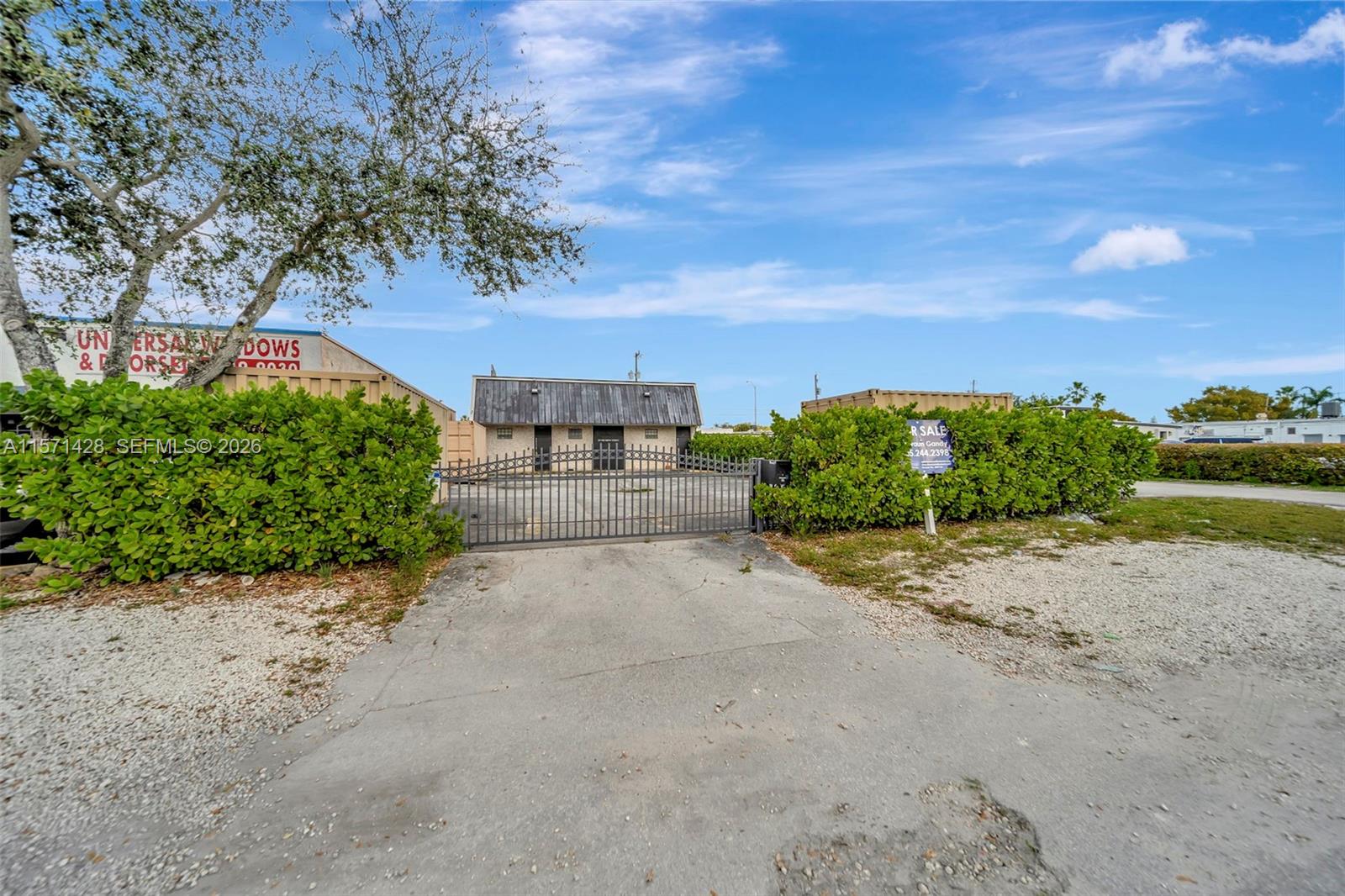 A gated concrete driveway leads to a small commercial building behind a hedge — 67 NW 166th St, Miami FL 33169, MIAMI, FL