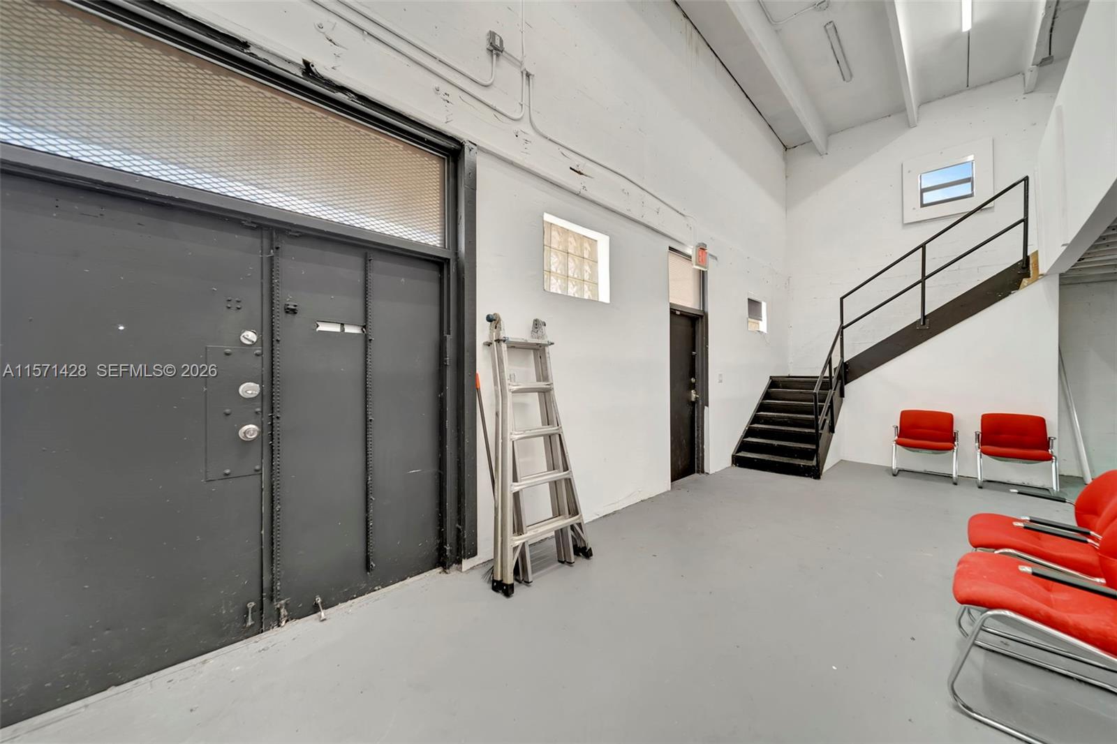 An industrial-style room features a large metal door, a staircase, and several red chairs — 67 NW 166th St, Miami FL 33169, MIAMI, FL