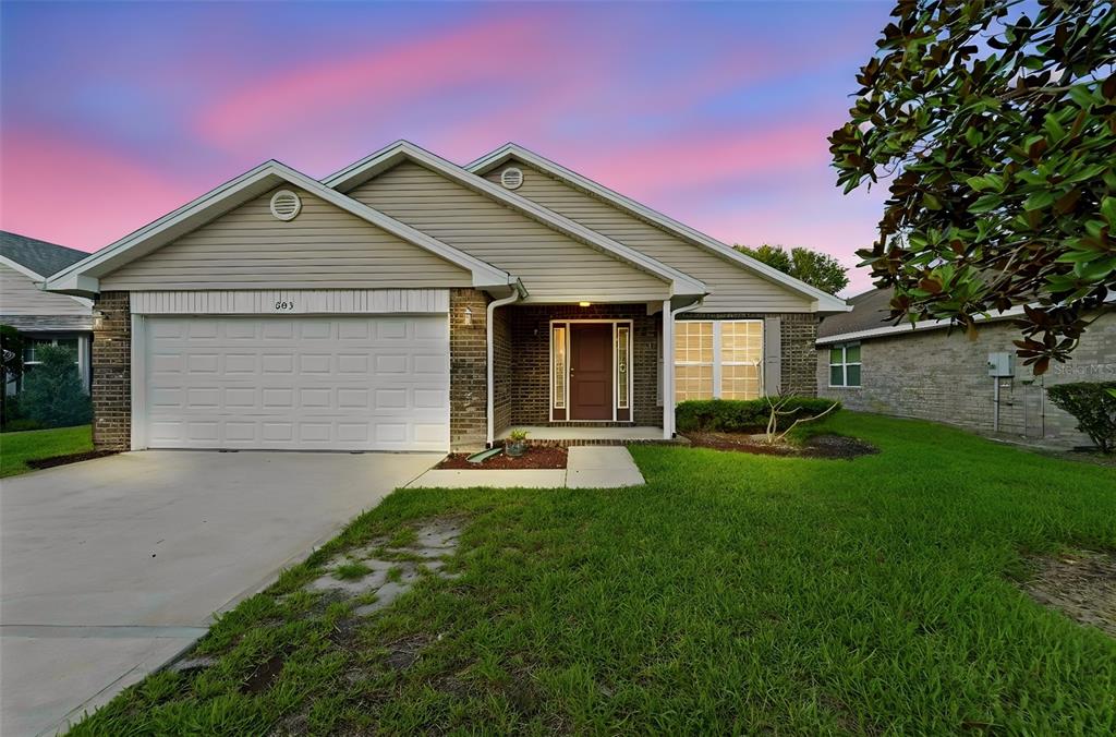A single-story house with a beige vinyl-sided facade, brick accents, and a two-car garage — 603 CORAL TRACE BOULEVARD, EDGEWATER, FL