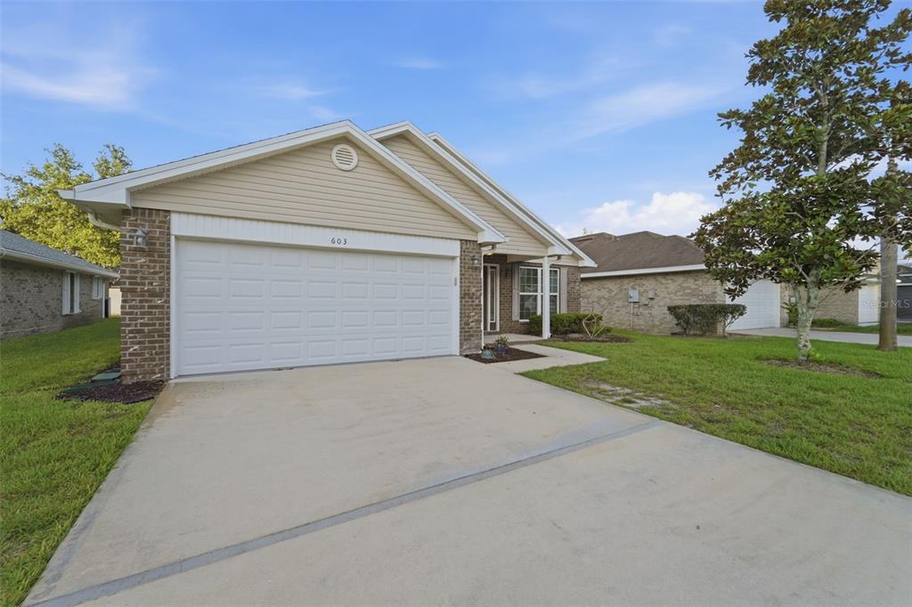 A single-story house with a beige vinyl gable, brick facade, and a two-car garage — 603 CORAL TRACE BOULEVARD, EDGEWATER, FL