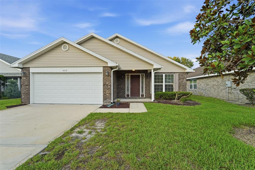 A single-story house with a beige vinyl-sided exterior, brick accents, and a two-car garage — 603 CORAL TRACE BOULEVARD, EDGEWATER, FL