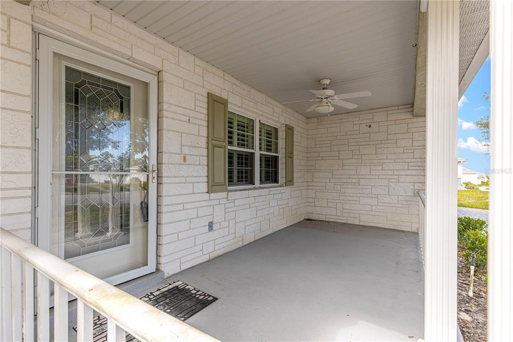 A covered front porch features white stone walls, a ceiling fan, and a glass storm door — 9878 SW 97TH LANE, OCALA, FL