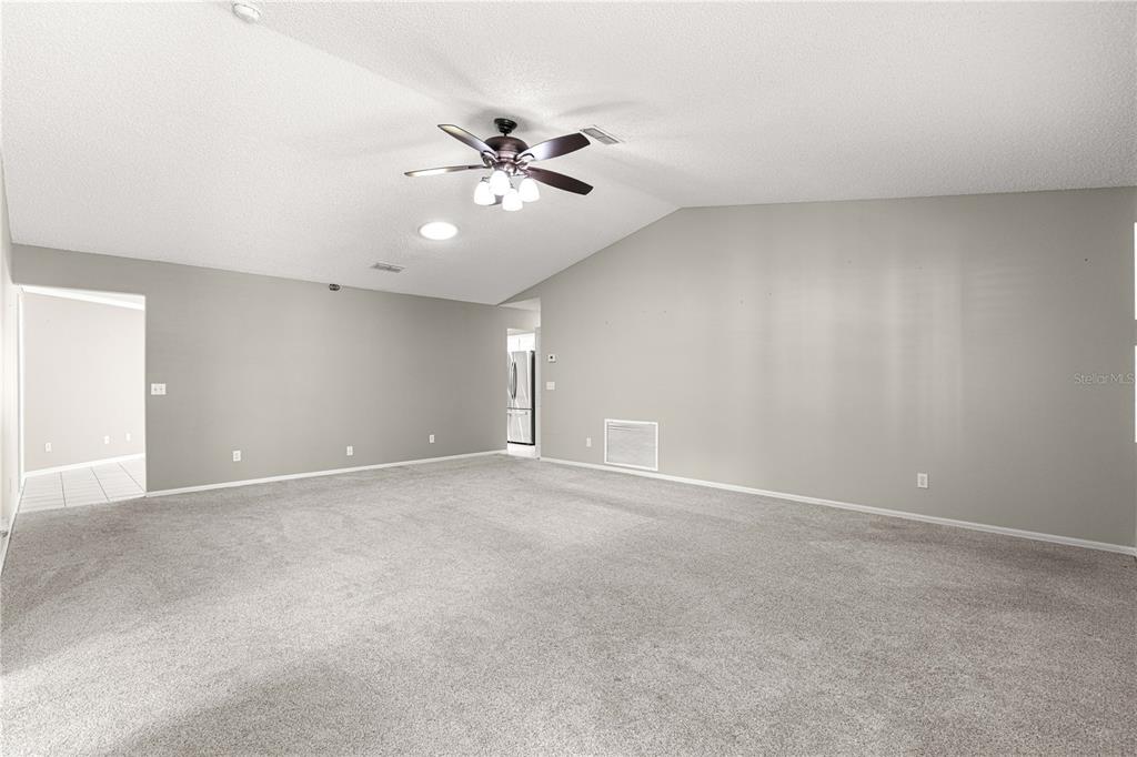 A spacious living room features gray walls, neutral carpeting, and a vaulted ceiling with a fan — 9878 SW 97TH LANE, OCALA, FL