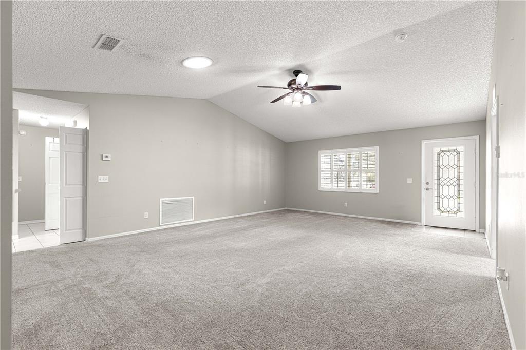 A spacious living room features gray carpeting, light-colored walls, a vaulted ceiling, and a ceiling fan — 9878 SW 97TH LANE, OCALA, FL