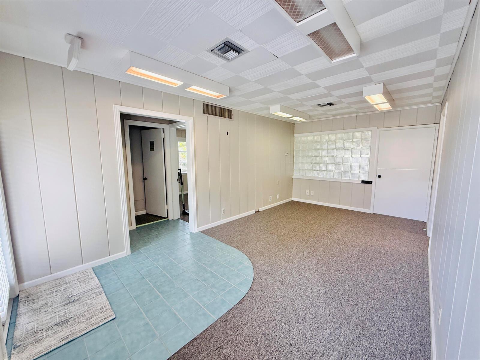 An interior room features a blue tiled entryway, carpeted flooring, wood-paneled walls, and glass block windows — 218 SE Osceola Street, Stuart FL 34994, STUART, FL