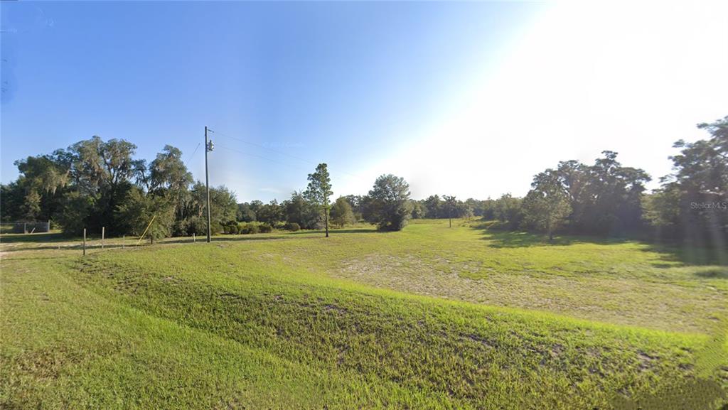A wide, grassy, undeveloped lot features scattered trees and a utility pole under a clear sky — TBD COMMERCE STREET, BRONSON, FL