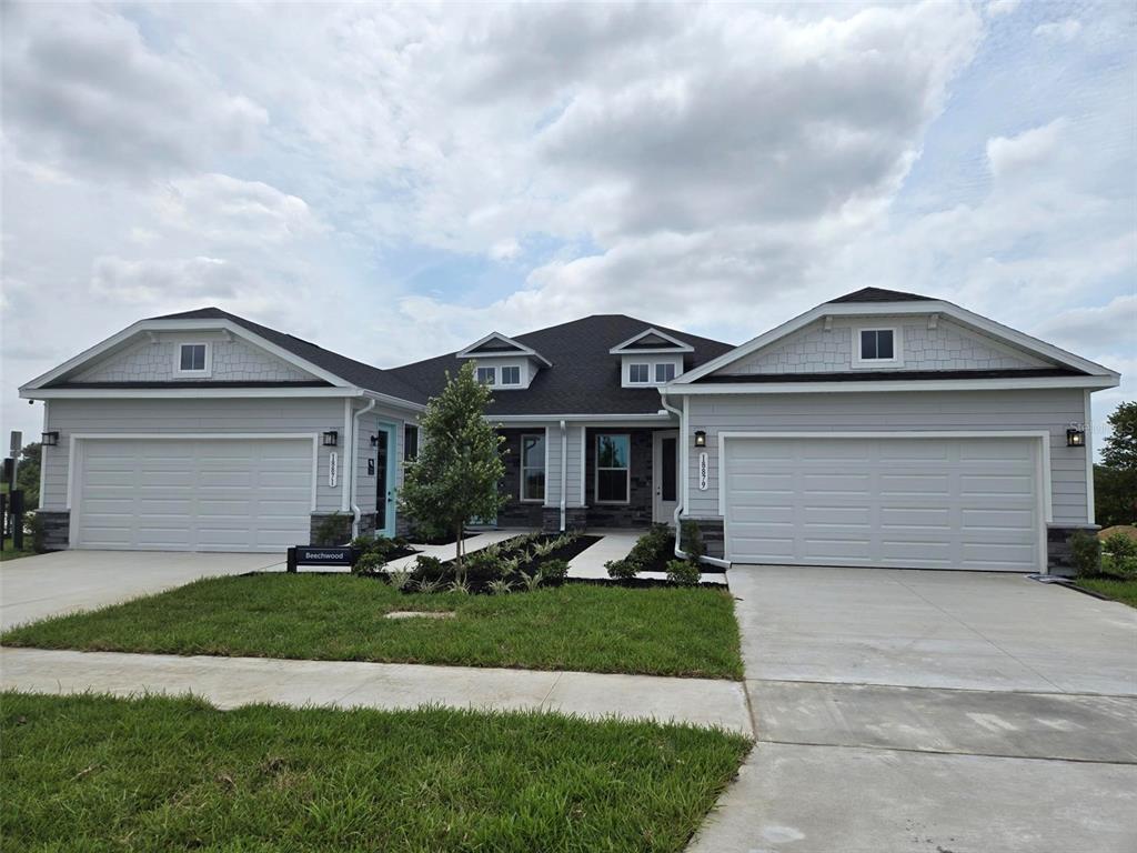 A duplex home with light gray siding, two garage doors, and a central landscaped walkway — 18740 HIGHLAND DEW STREET, SPRING HILL, FL