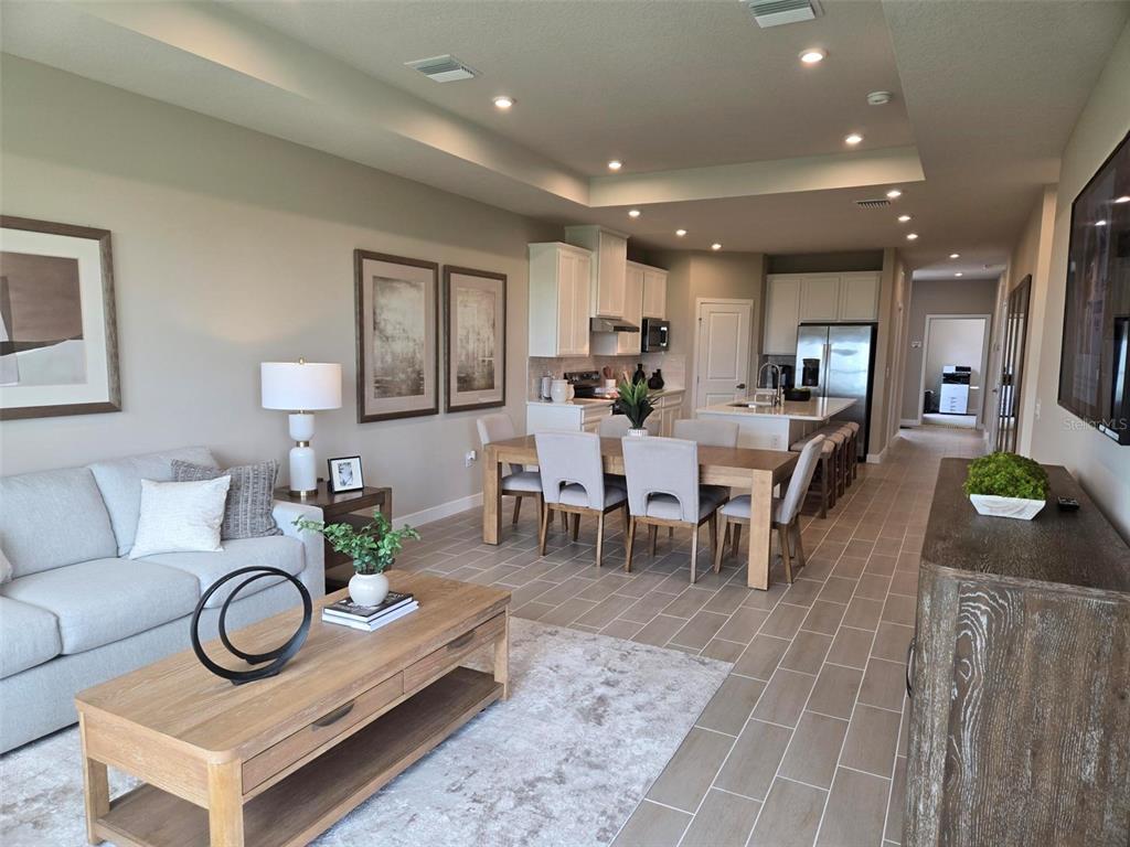 An open-concept living and dining area features light wood furniture, neutral decor, and tile flooring — 18740 HIGHLAND DEW STREET, SPRING HILL, FL