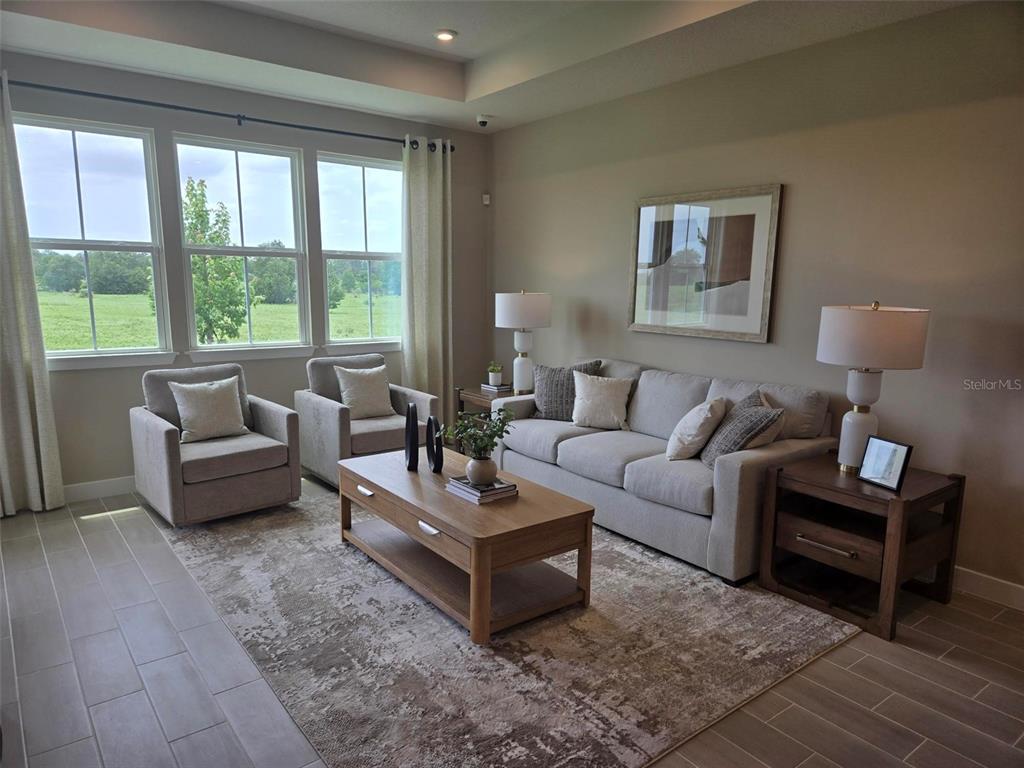 A living room features a light gray sofa, two armchairs, a wooden coffee table, and large windows — 18740 HIGHLAND DEW STREET, SPRING HILL, FL