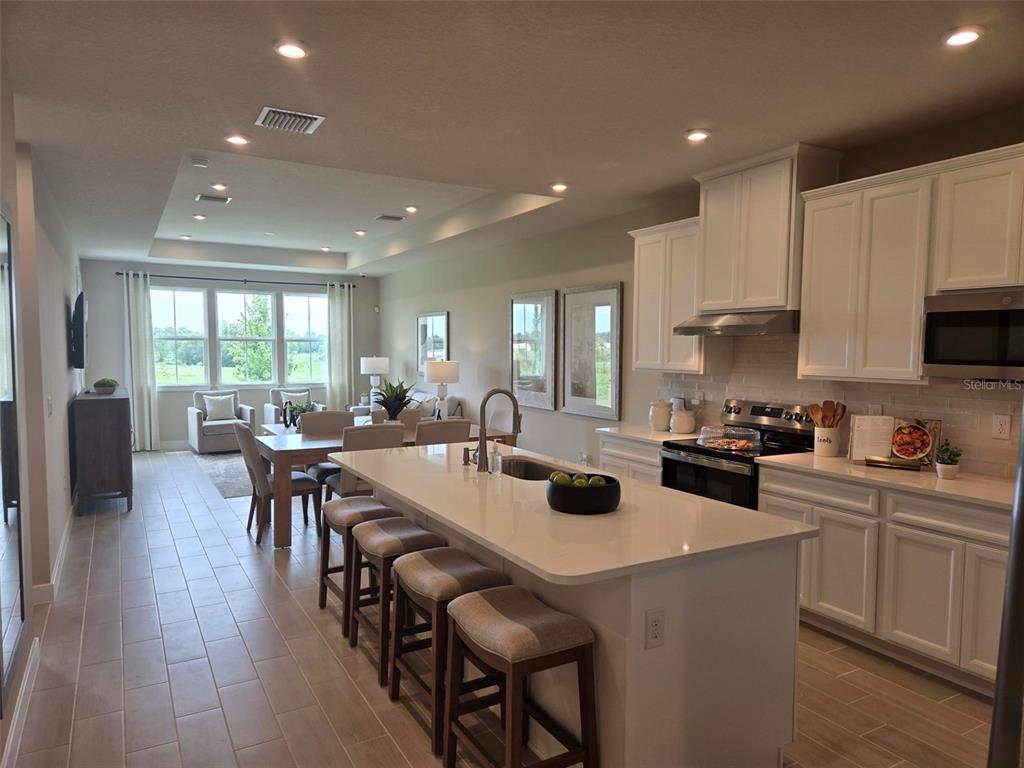A modern kitchen with white cabinets and a large island overlooks an open dining area — 18740 HIGHLAND DEW STREET, SPRING HILL, FL