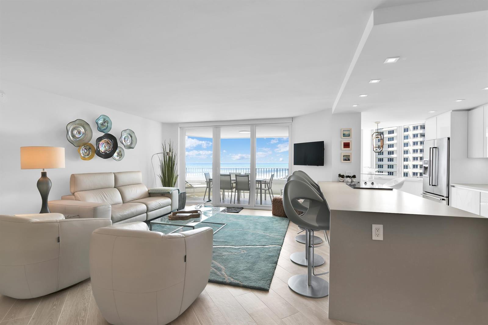 A modern living room and kitchen area features light wood floors, ocean views, and seating — 550 S Ocean Boulevard # 1004, Boca Raton FL 33432, BOCA RATON, FL