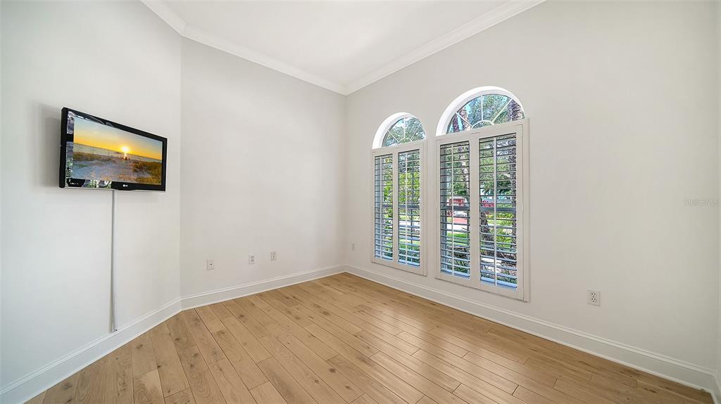 An empty room with light wood flooring, white walls, and two arched windows with shutters — 1704 FORTUNA STREET, SARASOTA, FL