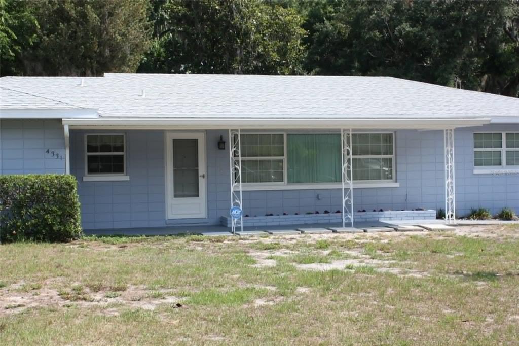 A light blue, single-story concrete block house with a covered front porch and white columns — 4331 MAGNOLIA AVENUE, LEESBURG, FL