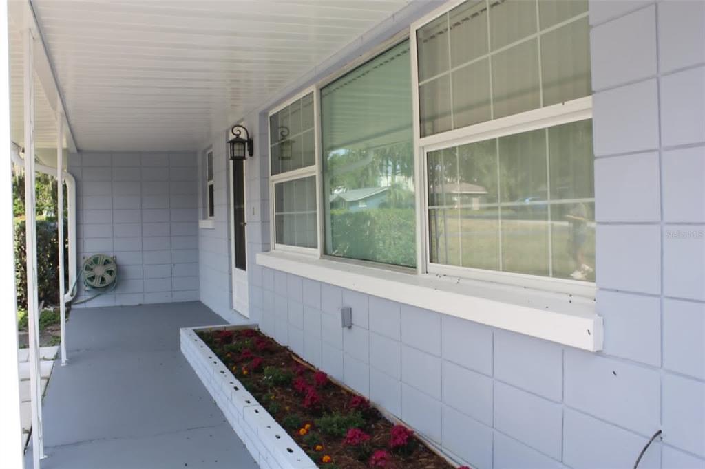 A covered porch with a concrete block wall, a flower bed, and large windows — 4331 MAGNOLIA AVENUE, LEESBURG, FL