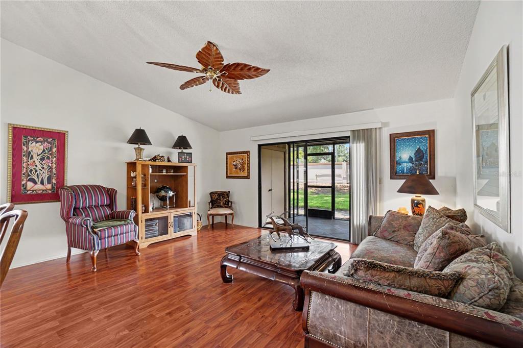 A living room features wood-look flooring, a ceiling fan, a patterned sofa, and sliding doors — 1708 CURRY TRAIL UNIT 3, NOKOMIS, FL