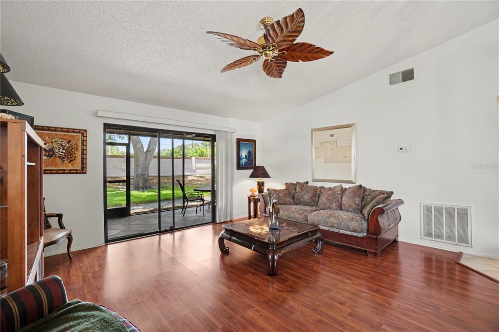 A living room features wood-look flooring, a ceiling fan, a patterned sofa, and sliding glass doors — 1708 CURRY TRAIL UNIT 3, NOKOMIS, FL