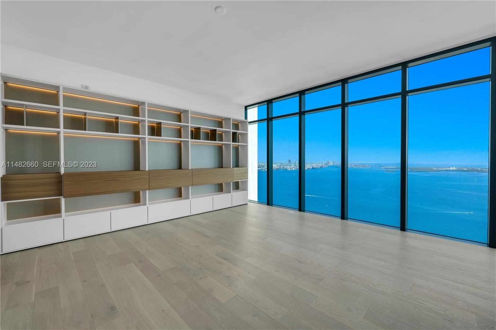 A modern room features light wood floors, a large built-in shelving unit, and floor-to-ceiling windows — 1451 Brickell Ave # 4403, Miami FL 33131, MIAMI, FL