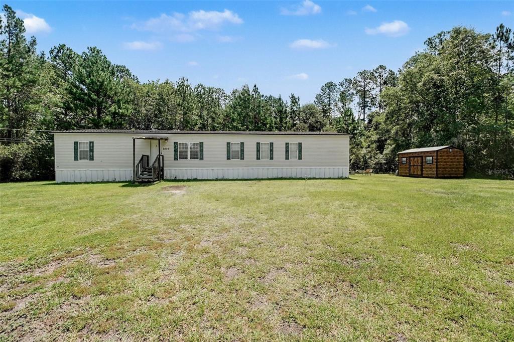 A single-story manufactured home sits on a grassy lot with a detached shed nearby — 2205 HIBISCUS AVENUE, MIDDLEBURG, FL