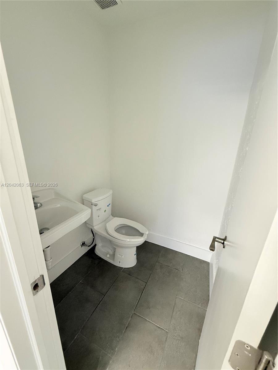 A small bathroom features a white toilet, a pedestal sink, and dark gray floor tiles — MEDLEY, FL