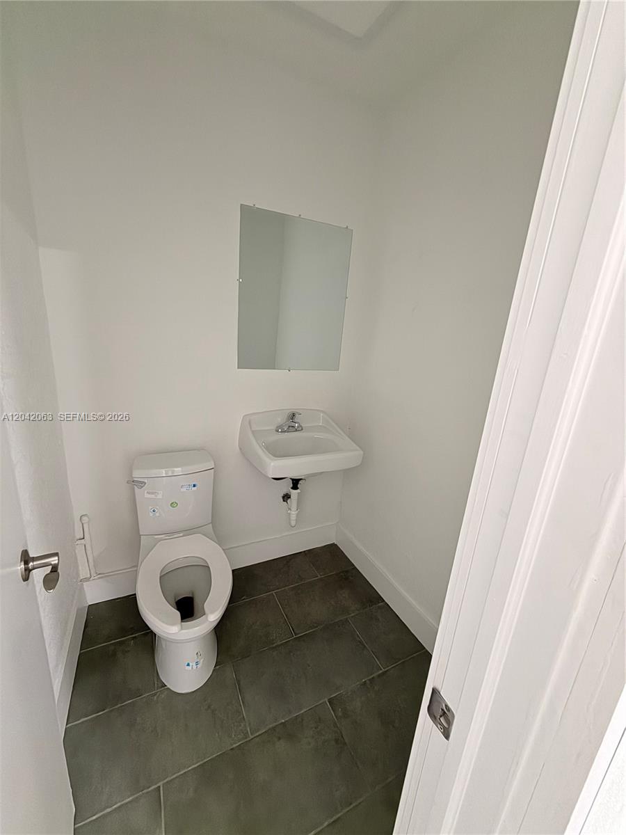 A small bathroom features a white toilet, a wall-mounted sink, and dark floor tiles — MEDLEY, FL