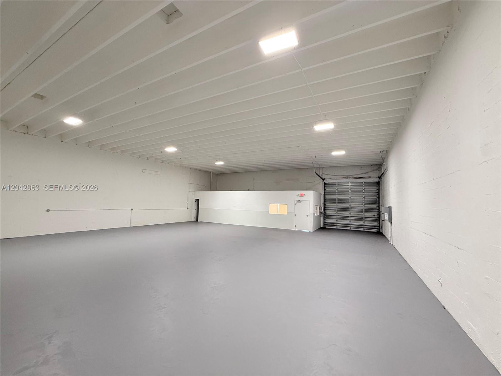 An empty industrial warehouse space features white walls, a gray floor, and a roll-up door — MEDLEY, FL