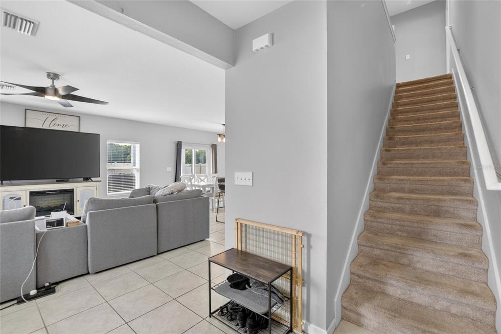 A living room with a gray sectional sofa, television, and carpeted stairs leading upward — 3706 ZEPHYR PRESERVE PLACE, ZEPHYRHILLS, FL