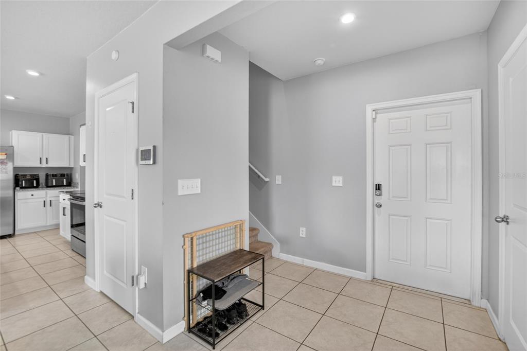 An entryway with tile flooring, a shoe rack, a staircase, and an adjacent kitchen — 3706 ZEPHYR PRESERVE PLACE, ZEPHYRHILLS, FL