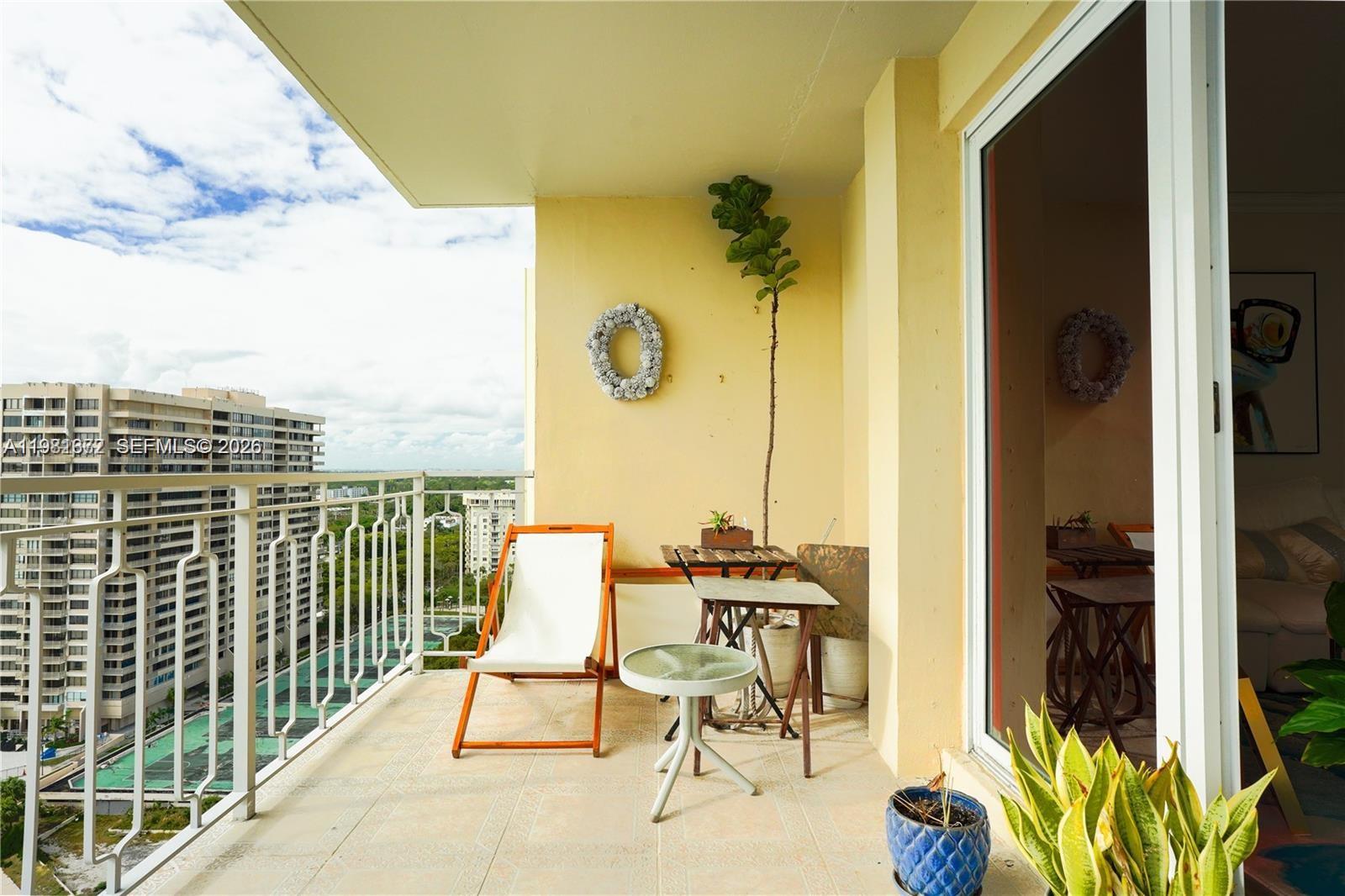 A balcony features a white lounge chair, small tables, potted plants, and a metal railing — 11111 Biscayne Blvd # 20E, Miami FL 33181, MIAMI, FL
