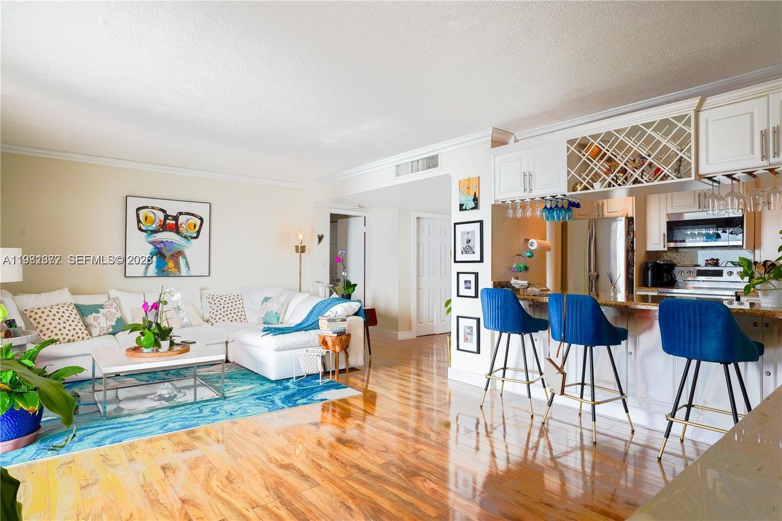 A living room with hardwood floors features a white sectional sofa and a kitchen bar — 11111 Biscayne Blvd # 20E, Miami FL 33181, MIAMI, FL