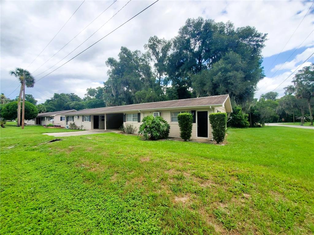 A single-story duplex with a tan exterior, a carport, and a large grassy yard — 5121-5115 UPSON AVENUE, DE LEON SPRINGS, FL