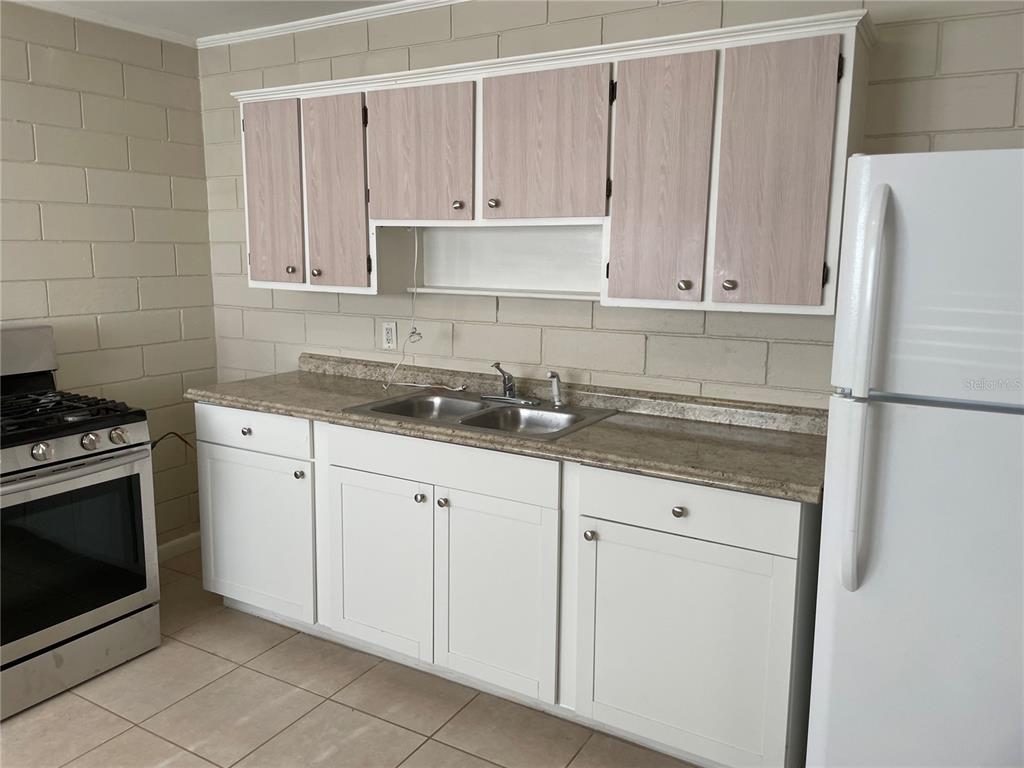 A kitchen features white lower cabinets, light wood-toned upper cabinets, a stainless sink, and appliances — 5121-5115 UPSON AVENUE, DE LEON SPRINGS, FL