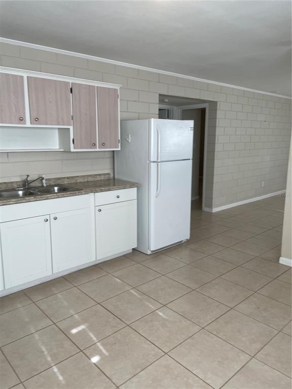 A kitchen features white lower cabinets, light wood-toned upper cabinets, a white refrigerator, and block walls — 5121-5115 UPSON AVENUE, DE LEON SPRINGS, FL