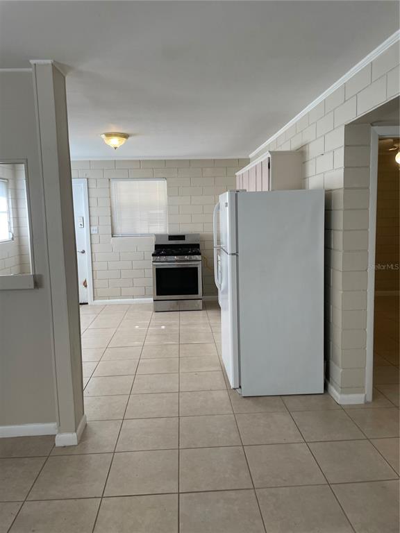 A kitchen features light-colored tile flooring, exposed concrete block walls, a white refrigerator, and a stove — 5121-5115 UPSON AVENUE, DE LEON SPRINGS, FL
