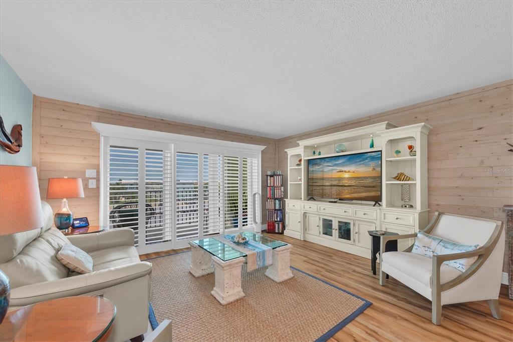 A living room features wood-paneled walls, a white entertainment center, and sliding glass doors — 420 64TH AVENUE UNIT 402E, ST PETE BEACH, FL