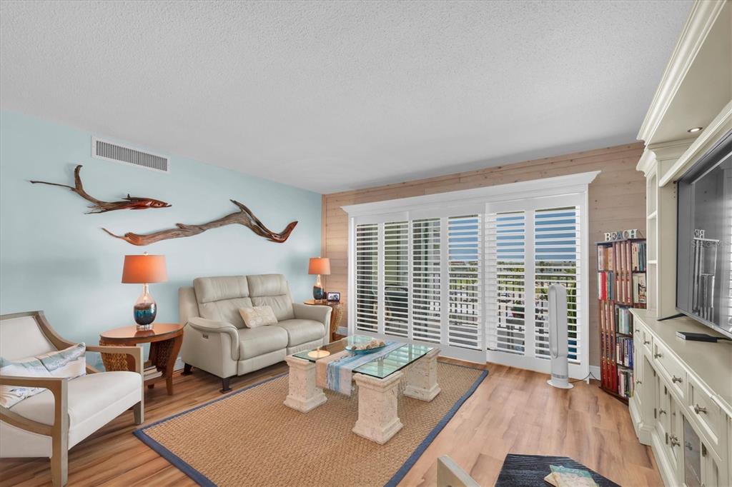 A living room features light blue walls, wood-look flooring, a beige sofa, and driftwood wall art — 420 64TH AVENUE UNIT 402E, ST PETE BEACH, FL