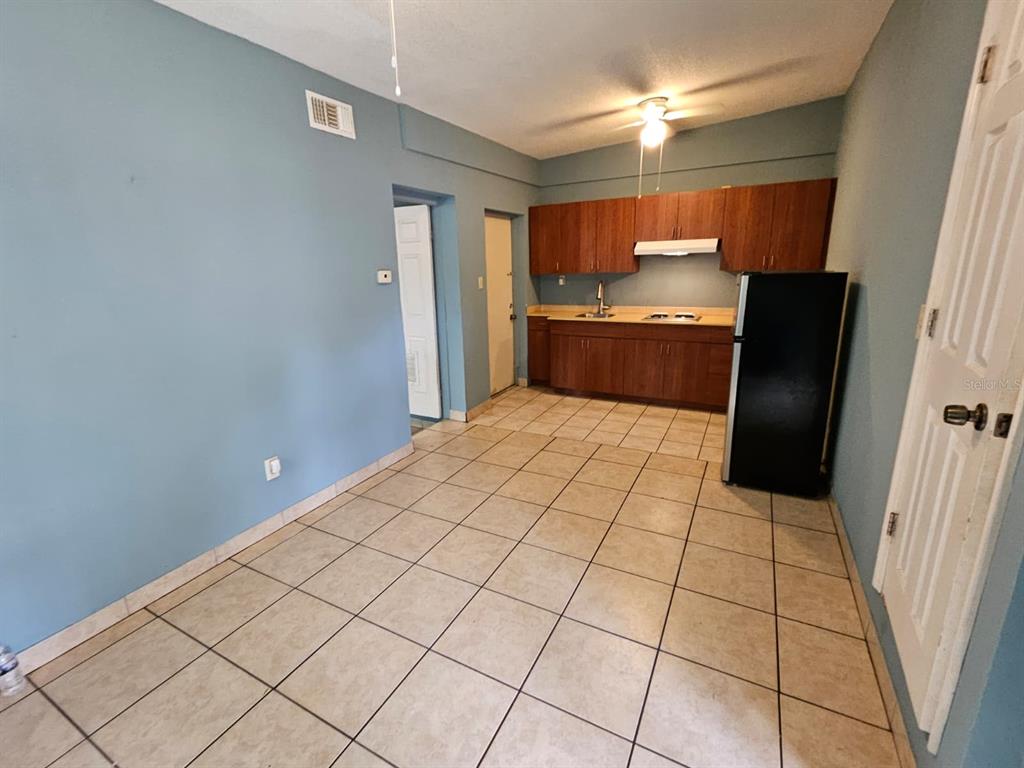 A kitchen features wood cabinets, a black refrigerator, and light-colored tile flooring — 118 N VAN BUREN AVENUE, ORLANDO, FL