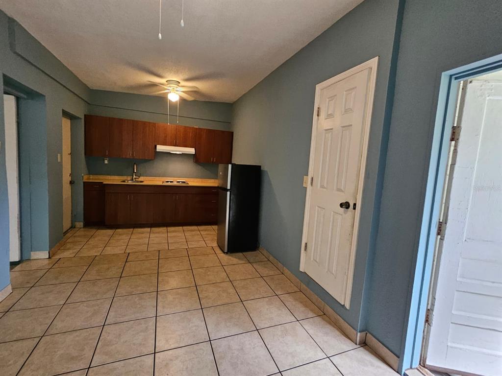 A kitchen with brown cabinets, tile flooring, and a black refrigerator against blue walls — 118 N VAN BUREN AVENUE, ORLANDO, FL