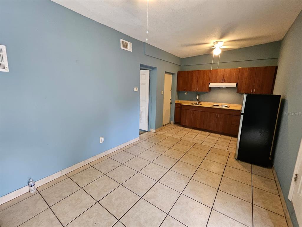 A kitchen with wood cabinets and a black refrigerator opens into a tiled living area — 118 N VAN BUREN AVENUE, ORLANDO, FL