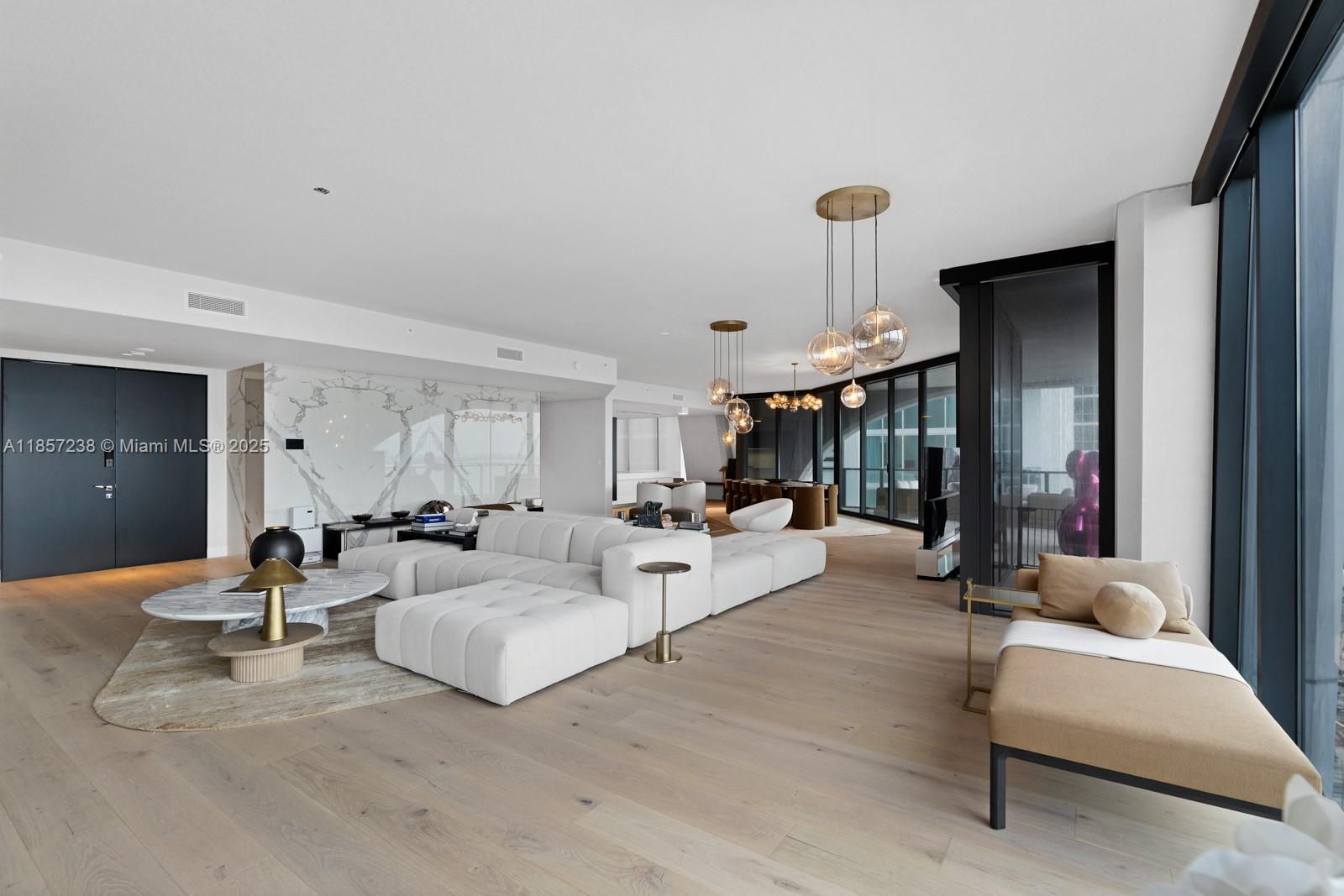 A modern living room features a white sectional sofa, marble wall, and floor-to-ceiling windows — 1000 Biscayne Blvd # 2402, Miami FL 33132, MIAMI, FL