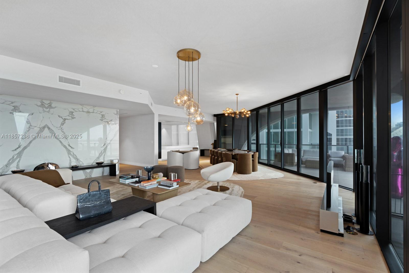 A modern living and dining area features a white sectional, marble wall, and floor-to-ceiling windows — 1000 Biscayne Blvd # 2402, Miami FL 33132, MIAMI, FL