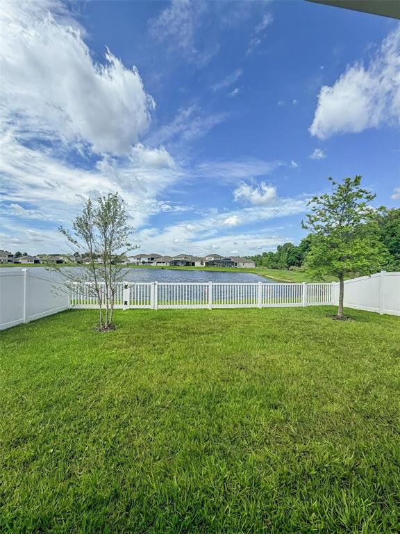 A grassy backyard features a white vinyl fence overlooking a lake and distant houses — 639 TERRAPIN DRIVE, DEBARY, FL