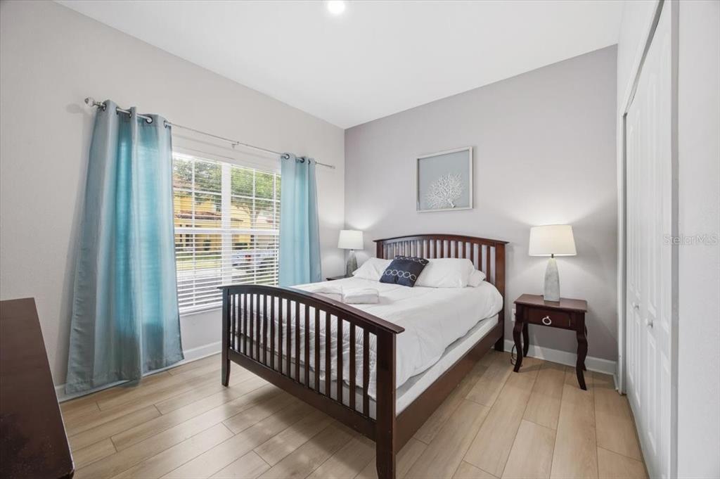 A bedroom features a wooden bed frame, light wood-look flooring, and blue curtains — 8922 CUBAN PALM ROAD, KISSIMMEE, FL