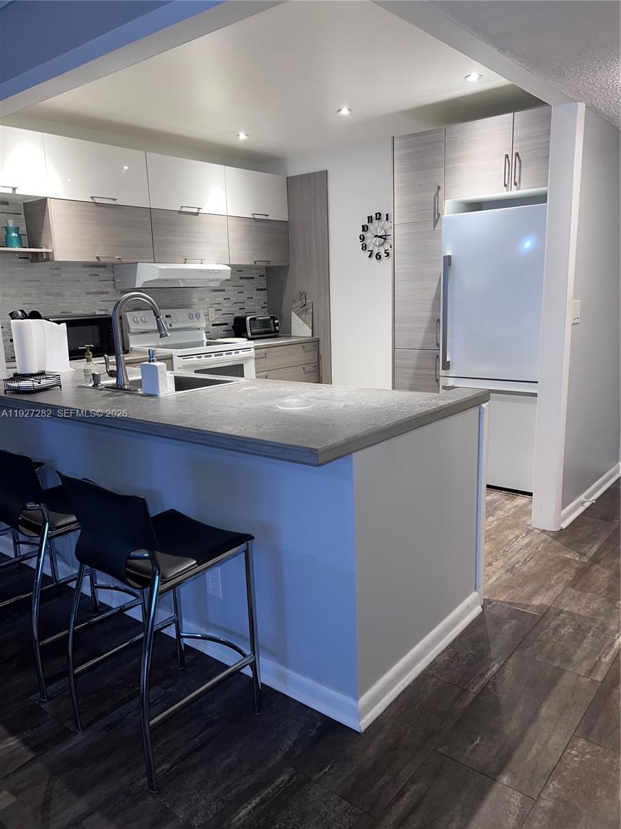 A kitchen features two-toned cabinetry, a gray countertop, a breakfast bar, and stainless steel appliances — 4740 NW 21st St # 4P, Lauderhill FL 33313, LAUDERHILL, FL