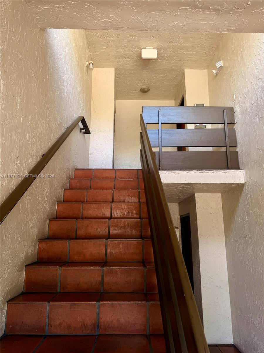 A staircase with terracotta tiles leads to an upper landing with a wooden railing — 8811 SW 123rd Ct # 1, Miami FL 33186, MIAMI, FL