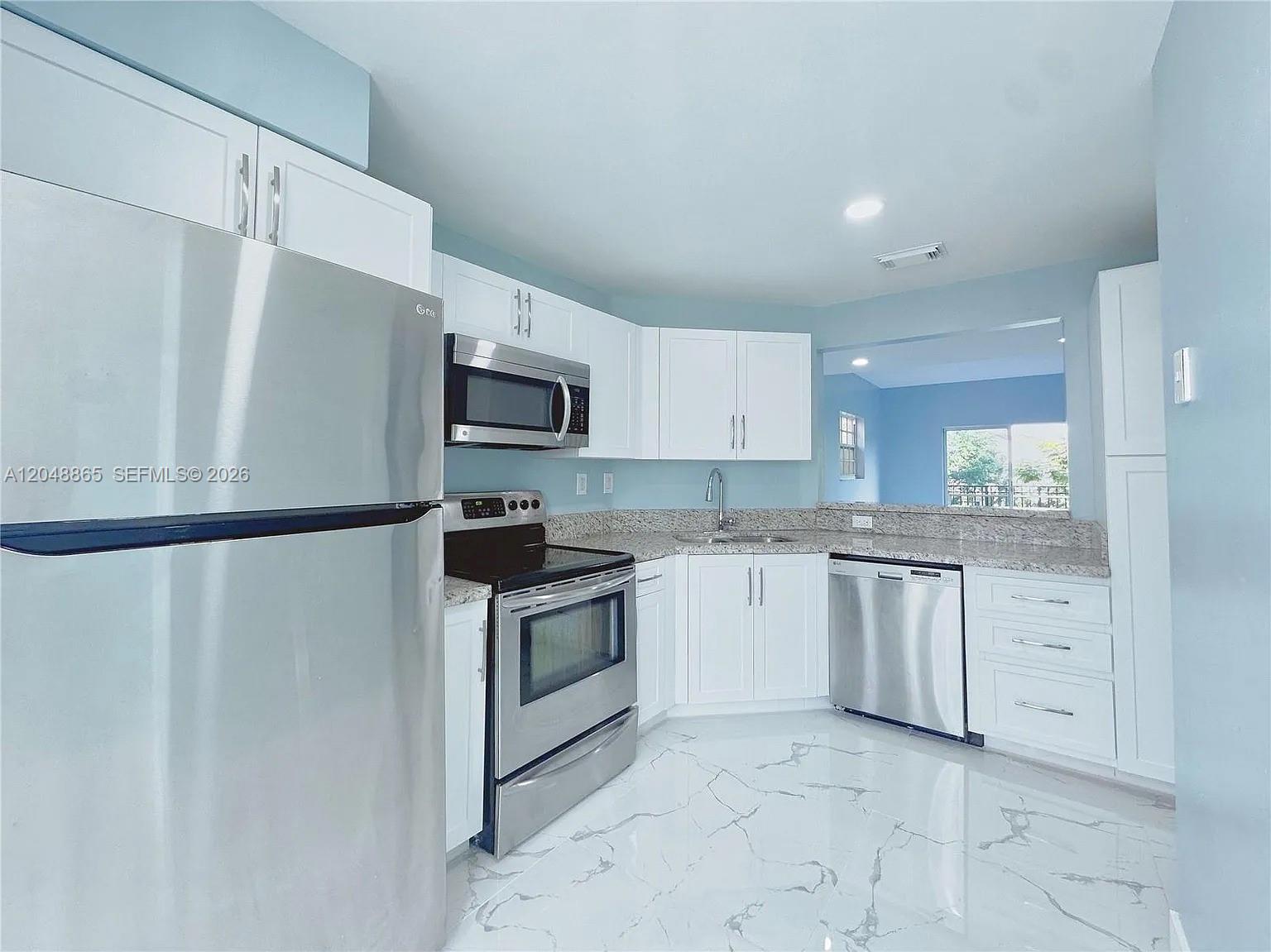 A kitchen features white cabinets, stainless steel appliances, granite countertops, and white marble-patterned tile flooring — 10014 Hammocks Blvd # 4, Miami FL 33196, MIAMI, FL