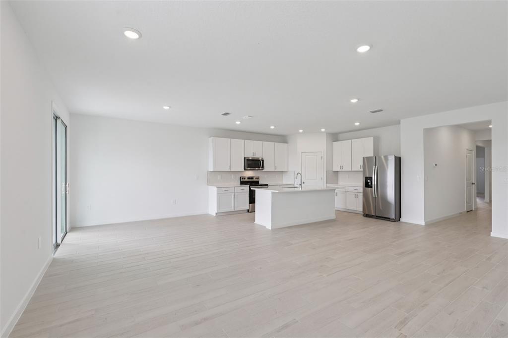 A bright, open-concept kitchen features white cabinetry, stainless steel appliances, and light wood-look flooring — 88 WANDERING CREEK WAY, PALM COAST, FL