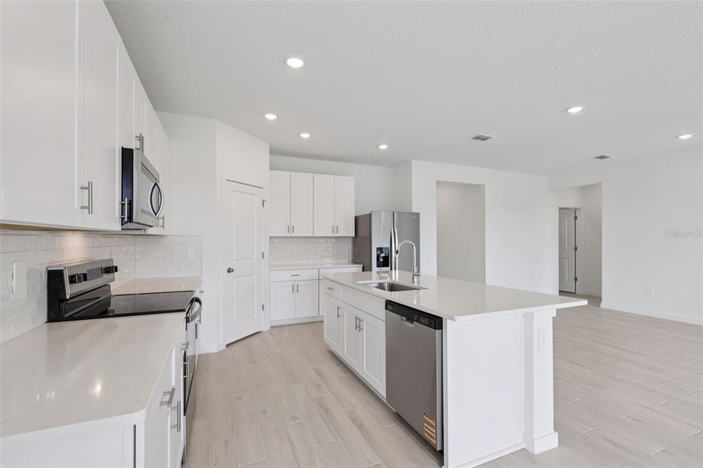 A modern kitchen features white cabinetry, quartz countertops, stainless steel appliances, and light wood flooring — 88 WANDERING CREEK WAY, PALM COAST, FL
