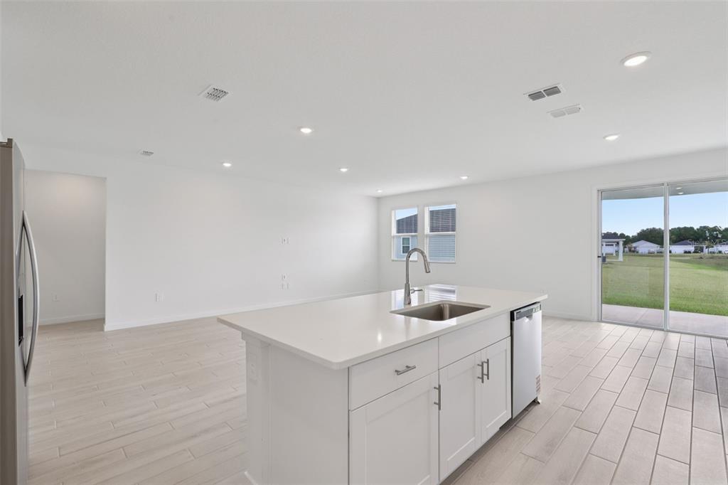 A bright kitchen features a white island with a sink, stainless dishwasher, and light flooring — 88 WANDERING CREEK WAY, PALM COAST, FL